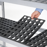 Person holding a black perforated mat over a metal shelf