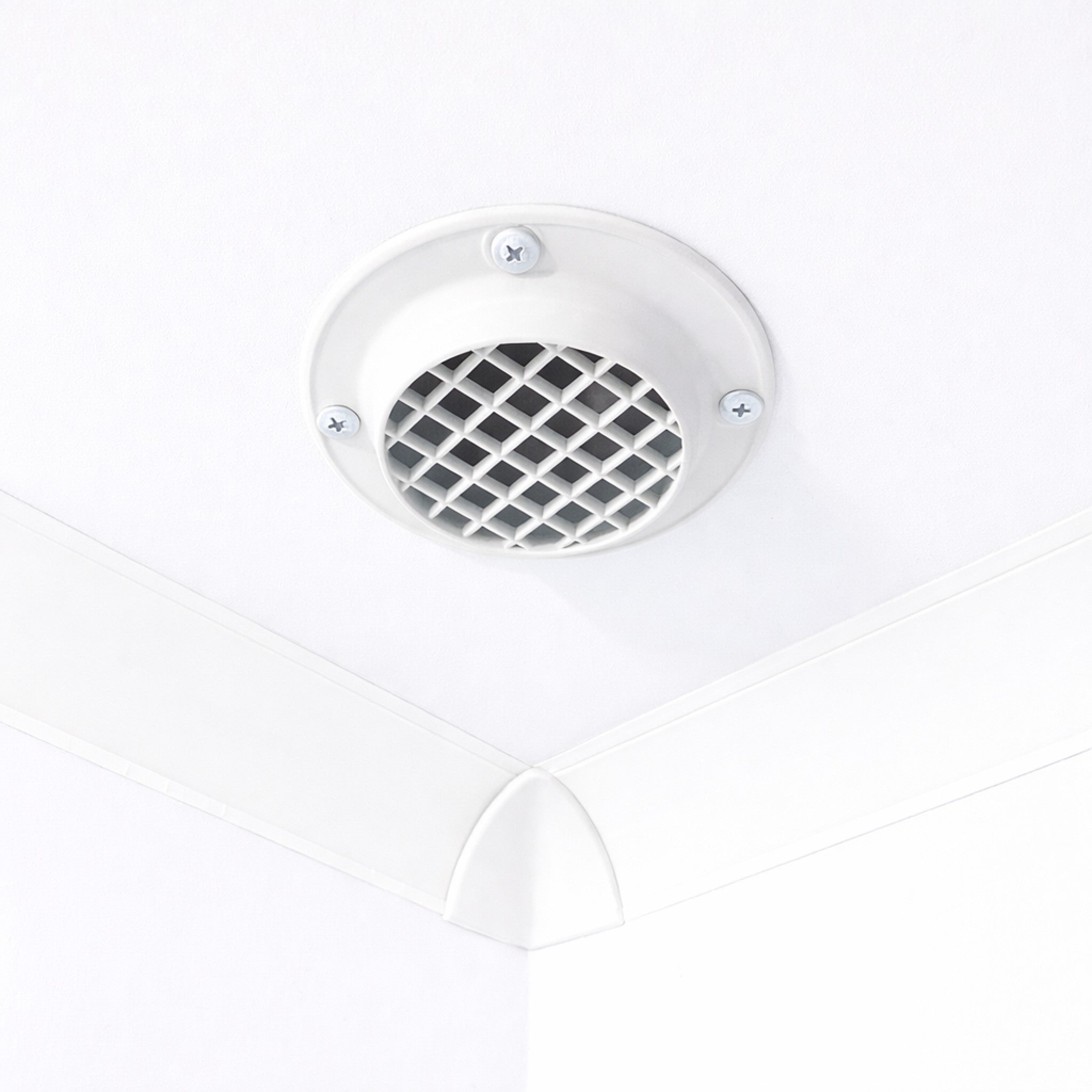 A white circular ceiling vent with a diamond-patterned grille, mounted on a white ceiling corner.